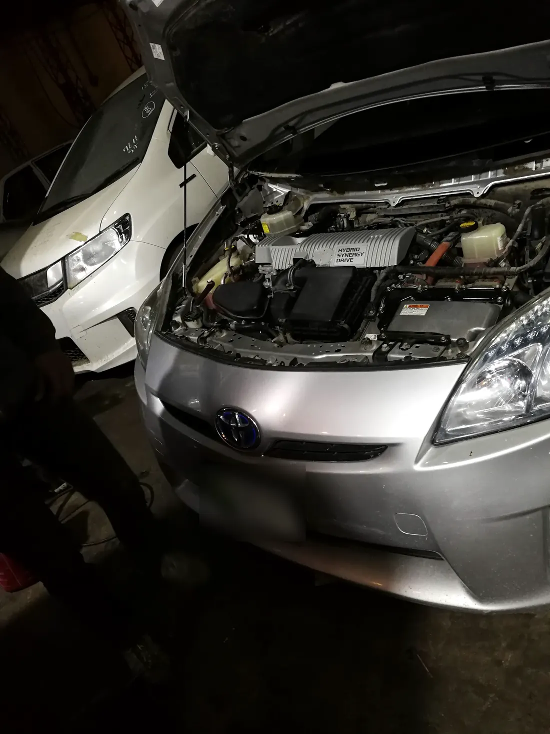 The engine bay of a Toyota Prius with its hybrid system cover, at the workshop